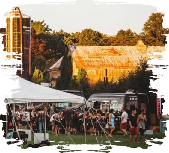 A crowd at an outdoor event beside the camper bar and a barn